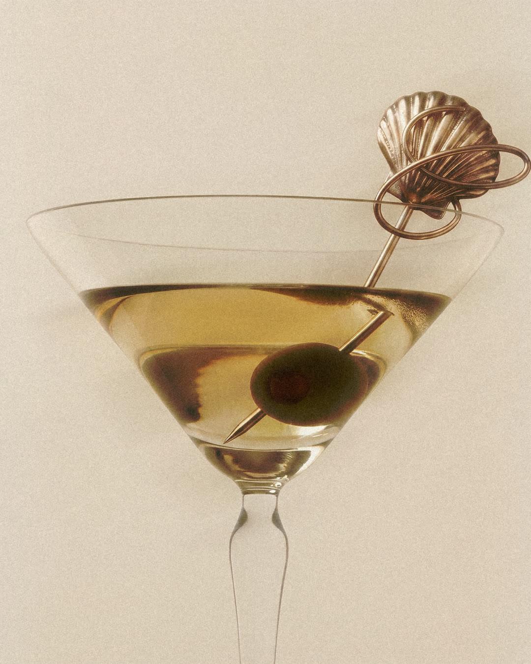 Un cocktail doré servi dans un verre à martini, avec une olive verte et un pique Caravelle